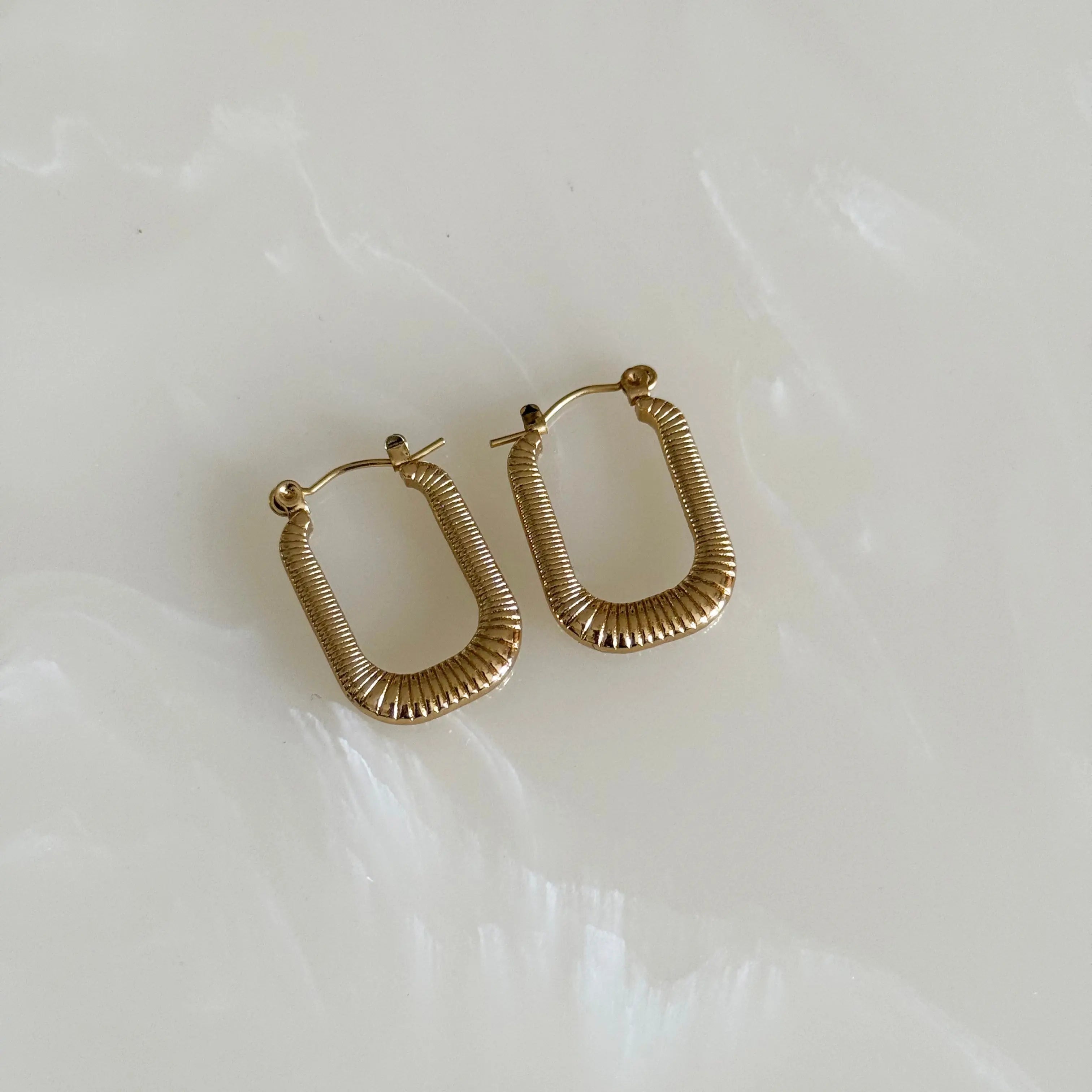 Gold hoop earrings on a light marble background